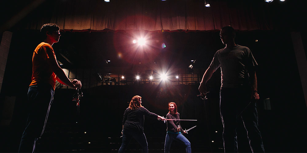Four theatre students performing on a dimly lit stage